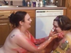 Two tattooed fat chicks play with food together in the kitchen